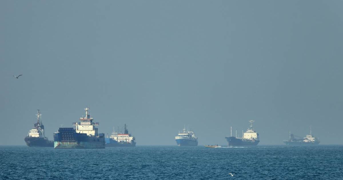 Cargo ships, including bulk carriers and general cargo vessels, sit at anchor offshore as a small motorboat passes in the foreground, in the Strait of Hormuz off Bandar Abbas, Iran, Monday, May 4 , 2026 (Amirhosein Khorgooi/ISNA via AP)
