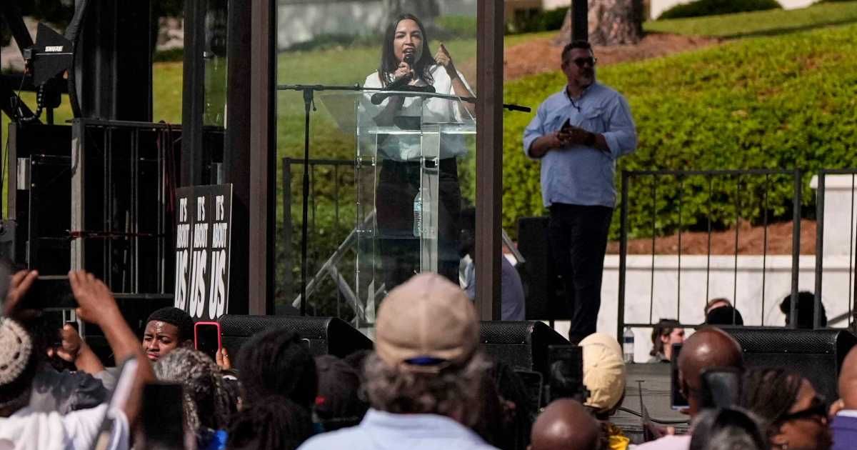 Rep Alexandria Ocasio-Cortez speaks from behind a bullet-resistant glass during a voting rights rally, Saturday, May 16, 2026, in Montgomery, Alabama (AP Photo/Mike Stewart)