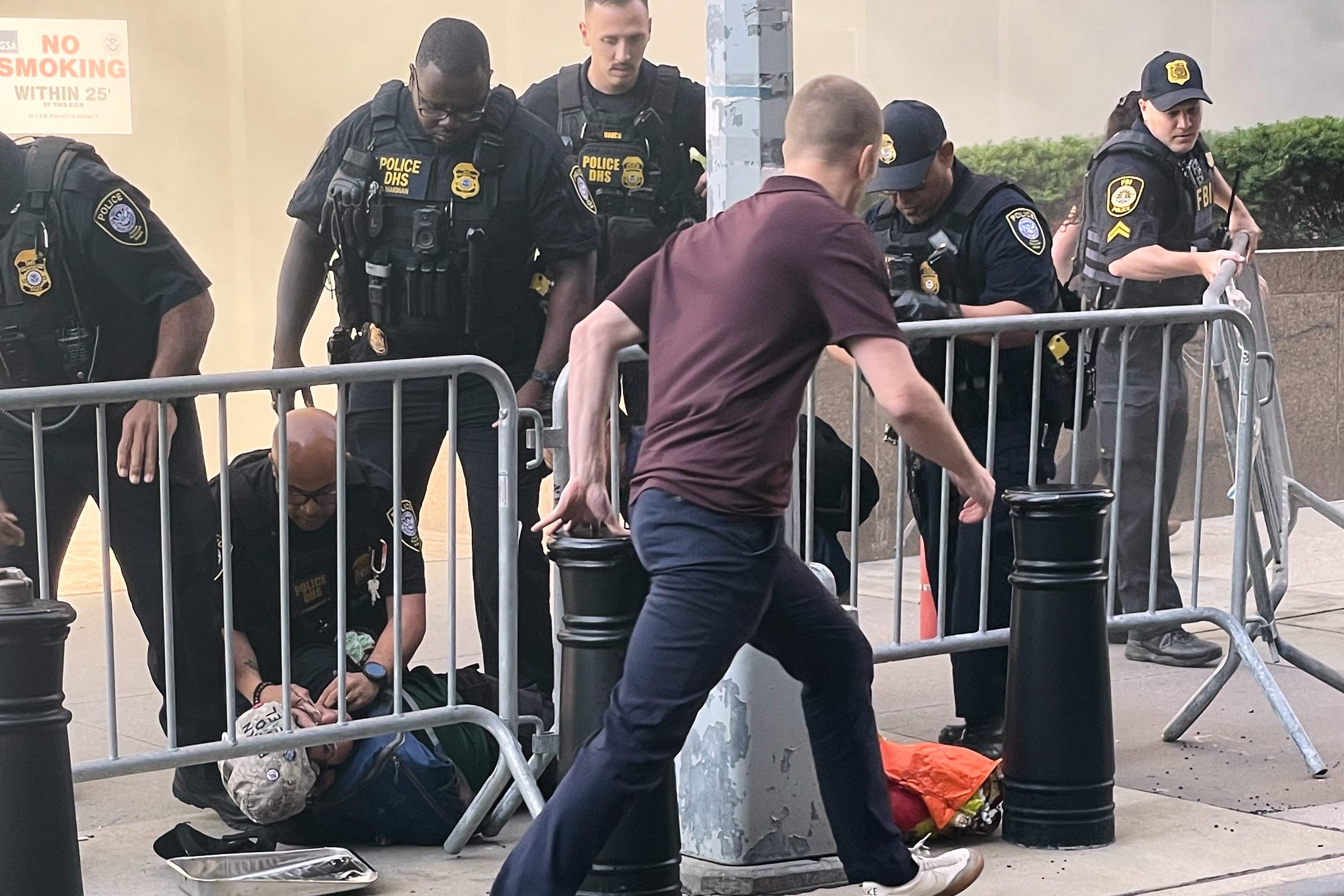 In this photo provided by Robert Sullivan several officers surround a person on the ground near the site of a fire at 26 Federal Plaza in lower Manhattan, Monday, July 20, 2026, in New York. (Robert Sullivan via AP)