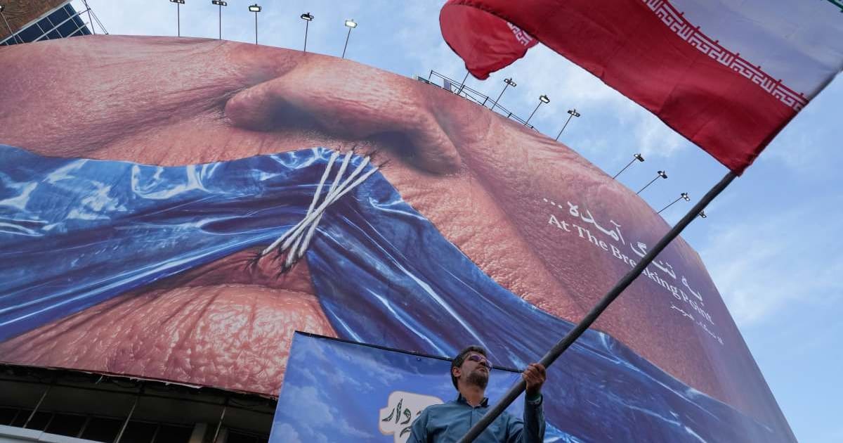 A man waves an Iranian flag for a pro-government campaign under a billboard with graphic showing Strait of Hormuz and sewn lips of President Donald Trump in a square in downtown Tehran, Iran, Wednesday, May 6, 2026 (AP Photo/Vahid Salemi)